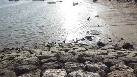Glückliches-Kind-Am-Sanur-Strandmeer,-Spielen-Im-Wasser-Unter-Goldenem-Sonnenuntergang,-Bali,-Indonesien,-Menschen-Genießen-Berühmtes-Asien-Reiseziel,-Boote-Angedockt