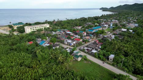 Luftaufnahme-Einer-Drohne-über-Dem-Kopf-Des-Malerischen-Barangay-Mit-Ruhiger-See-Im-Hintergrund-Und-üppigem-Grün-In-Catanduanes,-Philippinen