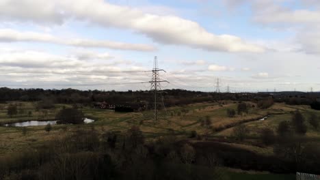 Electricity-distribution-power-pylon-overlooking-British-parkland-countryside,-Aerial-push-in-view