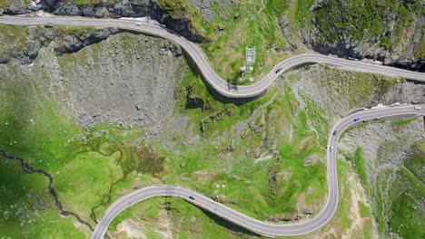 Top-Down-View-Of-Balea-Lake-And-The-Famous-Transfagarasan-Mountain-Road-In-Romania,-Aerial-View-Of-A-Beautiful-Mountain-Range-With-High-Peaks,-Thick-Fluffy-Clouds-And-A-Beautiful-Green-Valley