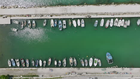 Aerial-top-down-footage-slowly-descending-showing-fishing-boats-docked-in-a-small-harbor-outside-of-old-city-Bari,-Italy