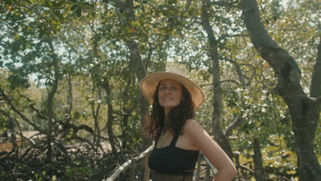 Slow-motion-shot-of-a-happy-brunette-European-woman-wearing-a-straw-hat-on-a-wooden-bridge-in-an-exotic-forest