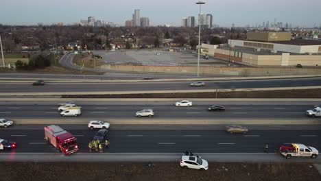 Aerial-footage-captures-the-fast-paced-action-of-emergency-responders-addressing-a-car-crash-on-a-busy-highway-during-the-day,-with-the-stunning-Toronto-skyline-in-the-background