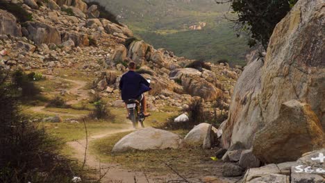 Free-young-man-rides-motorbike-on-dirt-path-through-rocky-landscape,-lone-travel