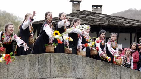 Hübsche-Bulgarische-Mädchen-In-Farbenfroher-Traditioneller-Kleidung-Führen-Das-Ritual-Durch,-Blumen-Von-Der-Brücke-In-Den-Fluss-Zu-Werfen