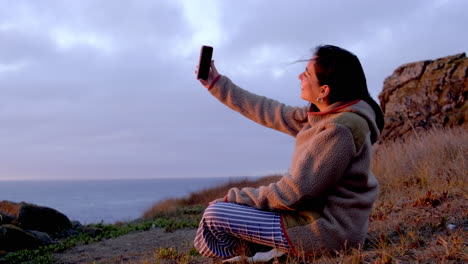 Mujer-Mirando-La-Cámara-De-Su-Teléfono-Celular,-Saludando-Y-Sonriendo,-Puesta-De-Sol-En-La-Playa,-Océano-Pacífico-Chile-Buchupureo