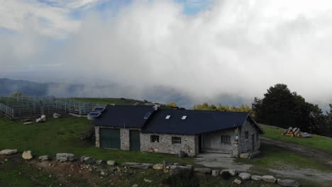 Farm-on-Prat-d'Albis-plateau-with-low-clouds-in-background,-Pyrenees-in-France