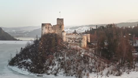Idyllic-Niedzica-Castle-at-dusk-on-top-of-hill-at-frozen-lake-Czorsztyn,-aerial