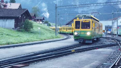 Gelber-Zug,-Der-Auf-Einer-Eisenbahn-Fährt,-Mit-Dem-Berg-Und-Den-Häusern-Im-Hintergrund