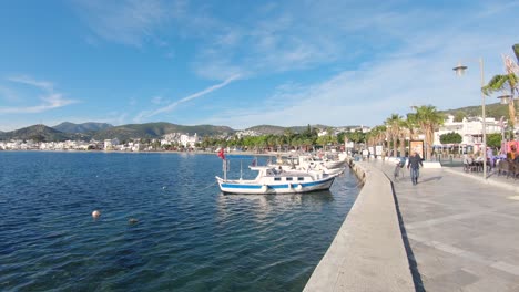 Man-walking,-fishing-boats-moored-along-promenade,-Bodrum,-Turkey