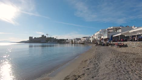 People-at-seaside-cafe-overlooking-Aegean-Sea-and-beach,-Bodrum,-Turkey