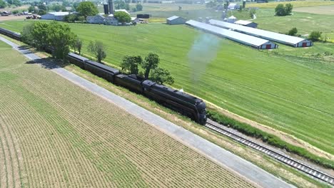 Eine-Drohnenansicht-Einer-Dampflokomotive-Mit-Personenwagen,-Die-Sich-An-Einem-Schönen-Sommertag-über-Die-Landschaft-Nähern
