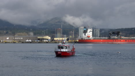 Dramatic-shot-of-cloudscape-surrounding-canadian-mountains-and-Red-fire-boat-cruising-on-water-in-foreground