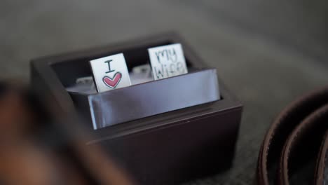 Close-up-slider-shot-of-groom-silver-cufflinks-in-a-dark-wooden-box-saying-I-love-my-wife