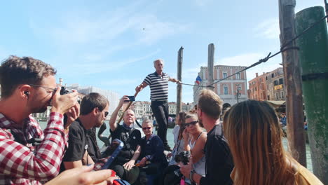Group-of-tourists-sitting-in-famous-gondola-and-old-standing-Gondolier-rowing-the-boat-on-the-river