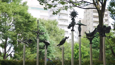 Estatuas-De-Criaturas-Japonesas-Se-Sientan-Entre-Los-árboles-En-Un-Tranquilo-Parque-De-Tokio-Con-Modernos-Bloques-De-Apartamentos-En-El-Fondo