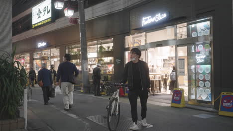 Hombre-Con-Máscara-Debajo-De-La-Barbilla-Caminando-Con-Bicicleta-En-La-Calle-De-Jiyugaoka-Durante-La-Pandemia-En-Tokio,-Japón
