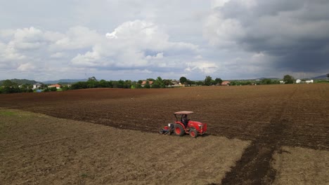 Static-shot-of-a-red-tractor-tilling-a-rich-fertile-soil,-moving-diagonally-leaving-furrows-contrasting-between-old-and-new-plowed-land-in-rural-countryside-in-Thailand,-Southeast-Asia