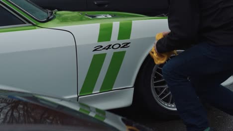 Man-Cleaning-Alloy-Wheel-Rim-on-Nissan-240z-Antique-Sports-Car-From-1970s-on-Auto-Show,-Slow-Motion