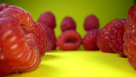 Macro-dolly-shot-of-several-ripe-raspberries-on-yellow-surface,-details-shot