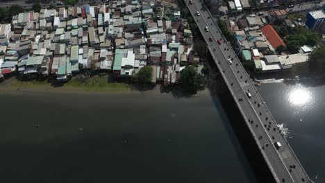 Aerial-shot-above-a-busy-traffic-bridge-and-waterfront-shanty-town-houses-along-Kenh-Te-canal-in-Ho-Chi-Minh-City,-Vietnam-on-a-sunny-day