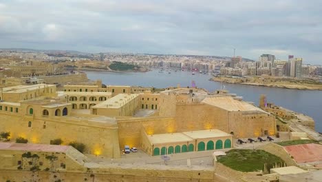 A-drone-flying-along-the-Grand-Harbour-from-Fort-St-Elmo-towards-the-Bell-Monument-at-Barrakka-Gardens-towards-in-Valletta-Malta
