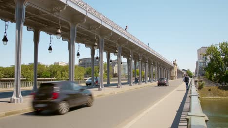 Menschen-Und-Fahrzeuge-Auf-Der-Straße,-Die-An-Einem-Sonnigen-Tag-An-Der-Historischen-Bir-Hakeim-Brücke-In-Paris,-Frankreich,-Vorbeifährt