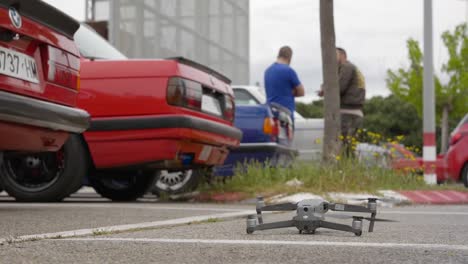 Beliebte-Drohne-Beginnt-Auf-Einem-Parkplatz-Mit-Autos-Und-Menschen-Zu-Fliegen