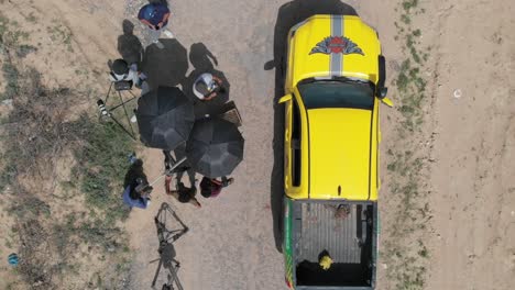 Aerial-Looking-Down-At-Parked-Yellow-4x4-Next-To-Small-Film-Crew-In-Desert