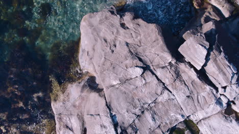 Drone-flying-over-cliffy-shore-with-clear-water