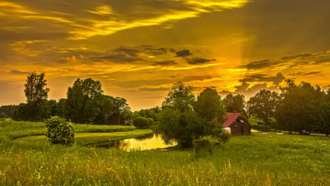 5k-Time-lapse-of-Sunbeams-shining-between-clouds-during-sunset-on-countryside-landscape-with-house-and-natural-lake---Sunset-Time-with-flying-cloudscape-in-green-scenery