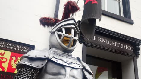 Medieval-imitation-knight-in-shining-silver-armour-standing-in-front-of-Welsh-heraldic-shop-closeup