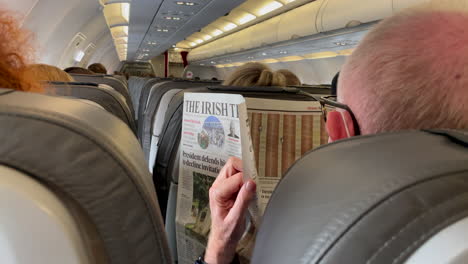 Rear-view-of-elderly-man-reading-Irish-newspaper-during-flight-in-airplane---close-up---Old-man-wearing-face-mask-during-covid-19-pandemic