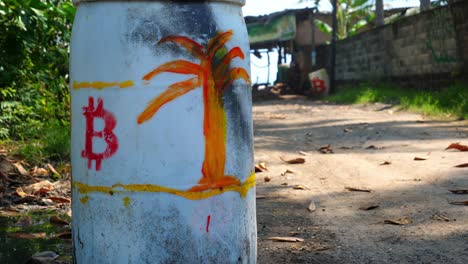 Full-shot,-a-white-drum-with-a-red-bitcoin-logo-and-orange-tree-drawing-on-the-bitcoin-beach-in-El-Salvador,-Mexico,-another-with-drum-with-a-bitcoin-logo-in-the-background
