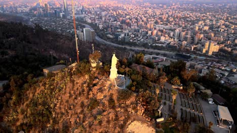 Aerial-parallax-of-statue-in-Sanctuary-of-the-Immaculate-Conception-in-San-Cristobal-Hill-top,-Santiago-city-in-background-at-sunset,-Chile
