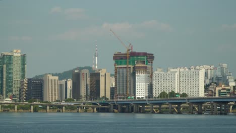 Hangang-River-waterfront-with-Cars-Traffic-on-Gangbyeon-Expressway-Road-,-Mapodaegyo-bridge-and-Mapo-gu-Urban-City-Skyline-with-Landmark-Seoul-Namsan-Tower-over-Blue-Sky,-South-Korea