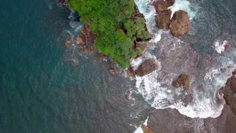 Aerial-top-down-shot-of-crashing-water-against-rocks-and-boulders-near-Jungwok-Beach,Indonesia