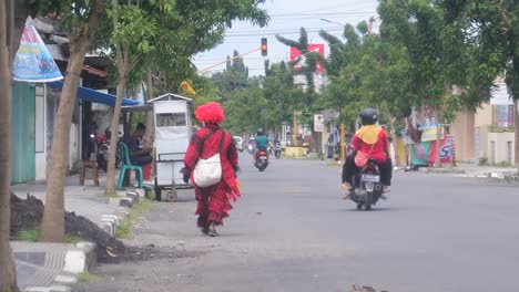 Un-Payaso-Con-Una-Camisa-Roja-Se-Aleja-Para-Buscar-Sustento-En-Una-Intersección-De-Luz-Roja-En-La-Carretera,-Blora,-Java-Central,-Indonesia,-21-De-Marzo-De-2022