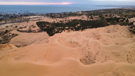 Vibrant-sandy-dunes-on-blue-coastline-of-Vietnam,-aerial-flying-view