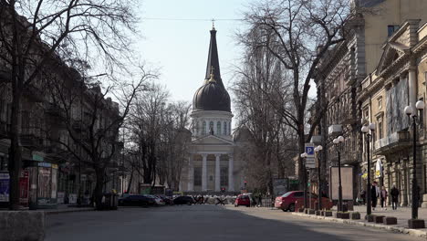 People-walk-past-a-distant-sandbag-barricade-and-tank-traps-in-front-of-an-ornate-church-during-the-Russian-invasion-of-Ukraine