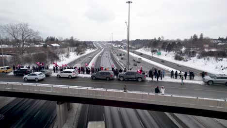 Canadian-Freedom-Rally-Protestors-waving-Canada-Flags,-standing-at-the-edge-of-highway-overpass-bridge-in-Toronto