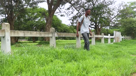 Slow-motion-shot-of-a-boy-in-blue-t-shirt-walking-towards-the-fence-and-jumping-over-it-in-the-park-and-smiling-in-environment-around-the-park-at-Harare,-Zimbabwe