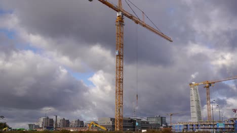 Blick-Auf-Zwei-Hohe-Kräne,-Die-Auf-Einer-Baustelle-Arbeiten,-Mit-Dramatischen-Wolken-Im-Hintergrund