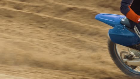 Motocross-Fahrer-Kommt-Von-Links-Ins-Bild,-Dreht-Den-Hinterreifen-Und-Versprüht-Sand-In-Zeitlupe