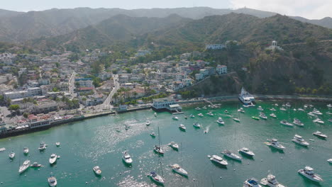 Beautiful-Avalon-Harbor-on-Catalina-Island-as-Seen-by-Drone,-Flying-Over-Sunny-Island-with-Docked-Boats-and-Rocky-Terrain