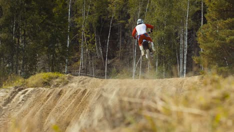 Motocross-rider-jumps-in-slow-motion-on-a-dirt-track-in-a-wooded-area