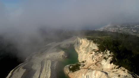 Aerial-View-Through-Rolling-Clouds-Of-Green-Toxic-Lake-At-Monte-Neme-Abandoned-Mine