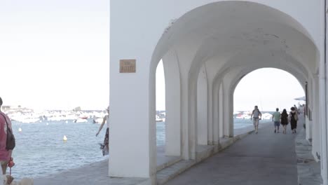 people-walking-on-a-sidewalk-near-the-sea-pier-in-Costa-Brava,-Cadaques,-Spain-on-May-24,-2022