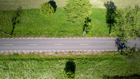 Aerial-drone-flying-over-lush-green-fields-next-to-the-road