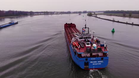 Aerial-Circle-Dolly-Around-Stern-Of-Wilson-Mosel-Cargo-Ship-Travelling-Along-Oude-Maas-On-Overcast-Day